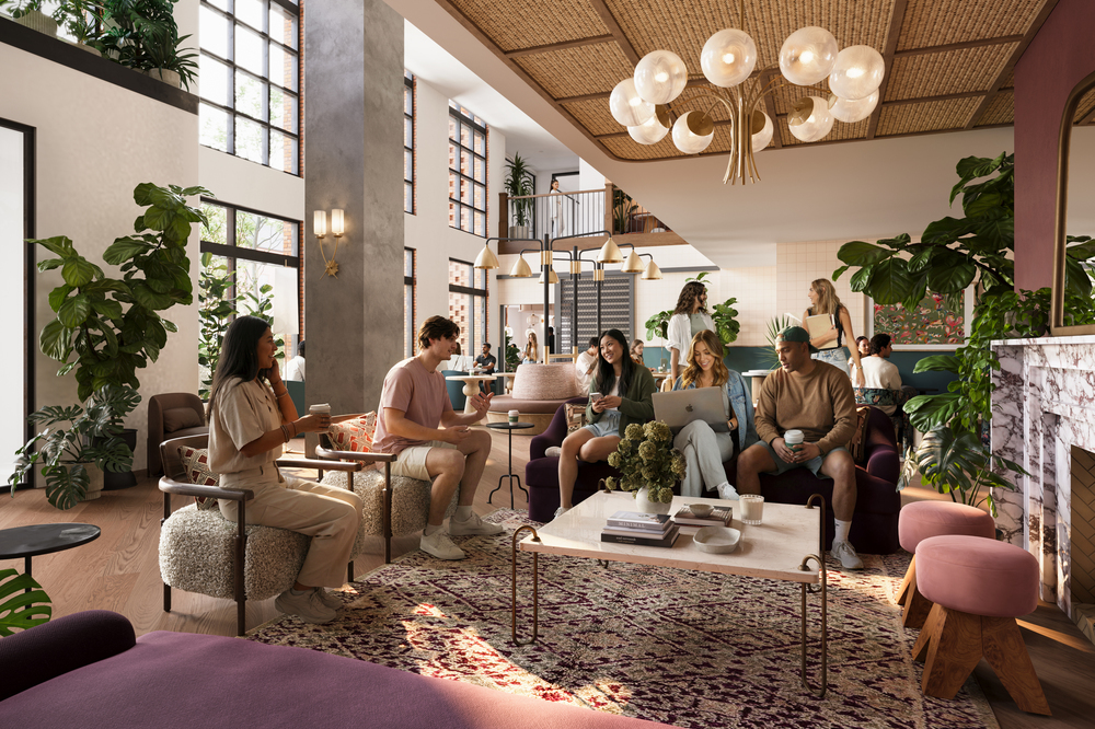 A group of young adults socialize in the stylish, sunlit Rambler Ann Arbor lounge with modern furniture, large windows, indoor plants, and a cozy atmosphere, featuring a fireplace and decorative lighting.